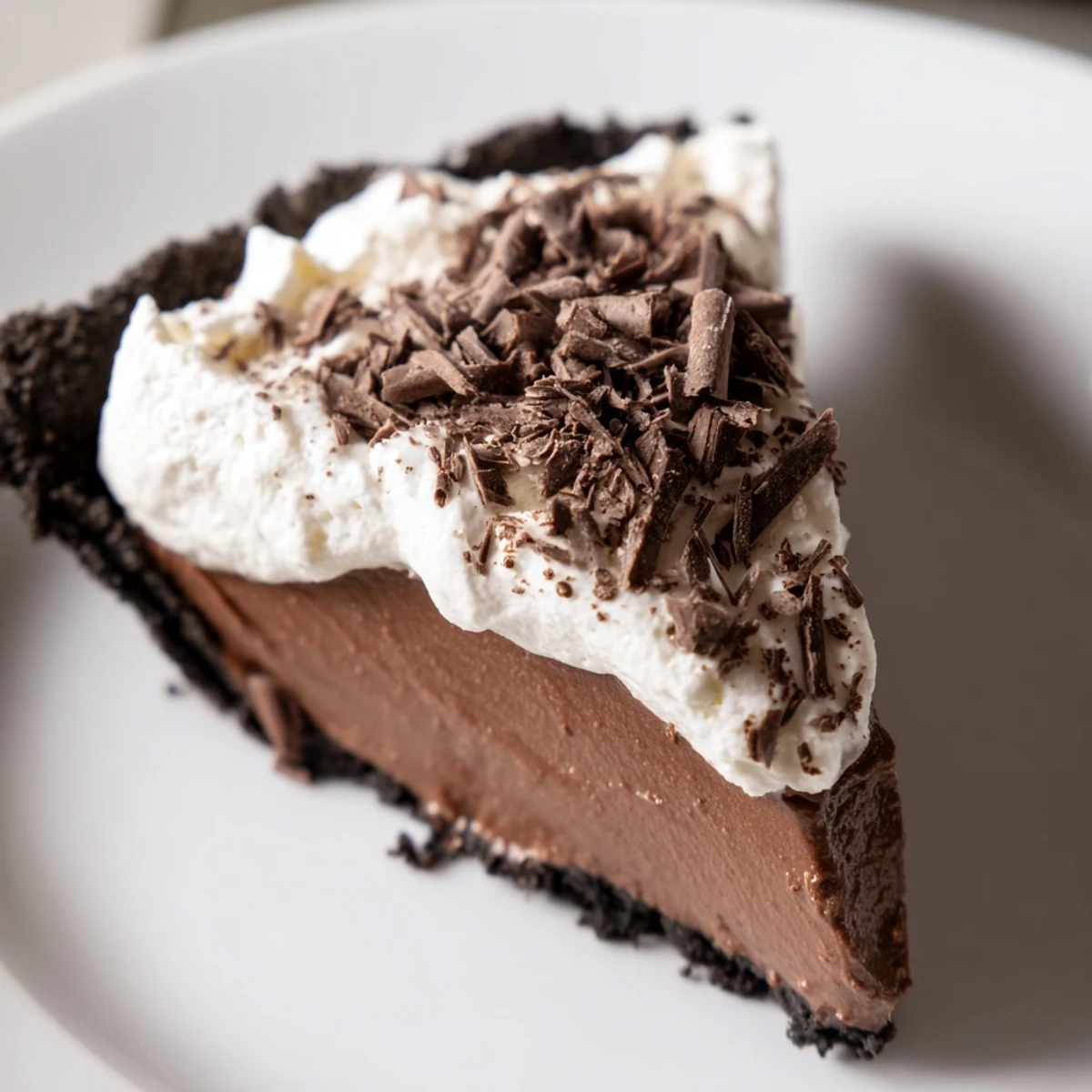 Slice of rich chocolate silk pie with whipped cream on a rustic wooden table, ideal for a party.