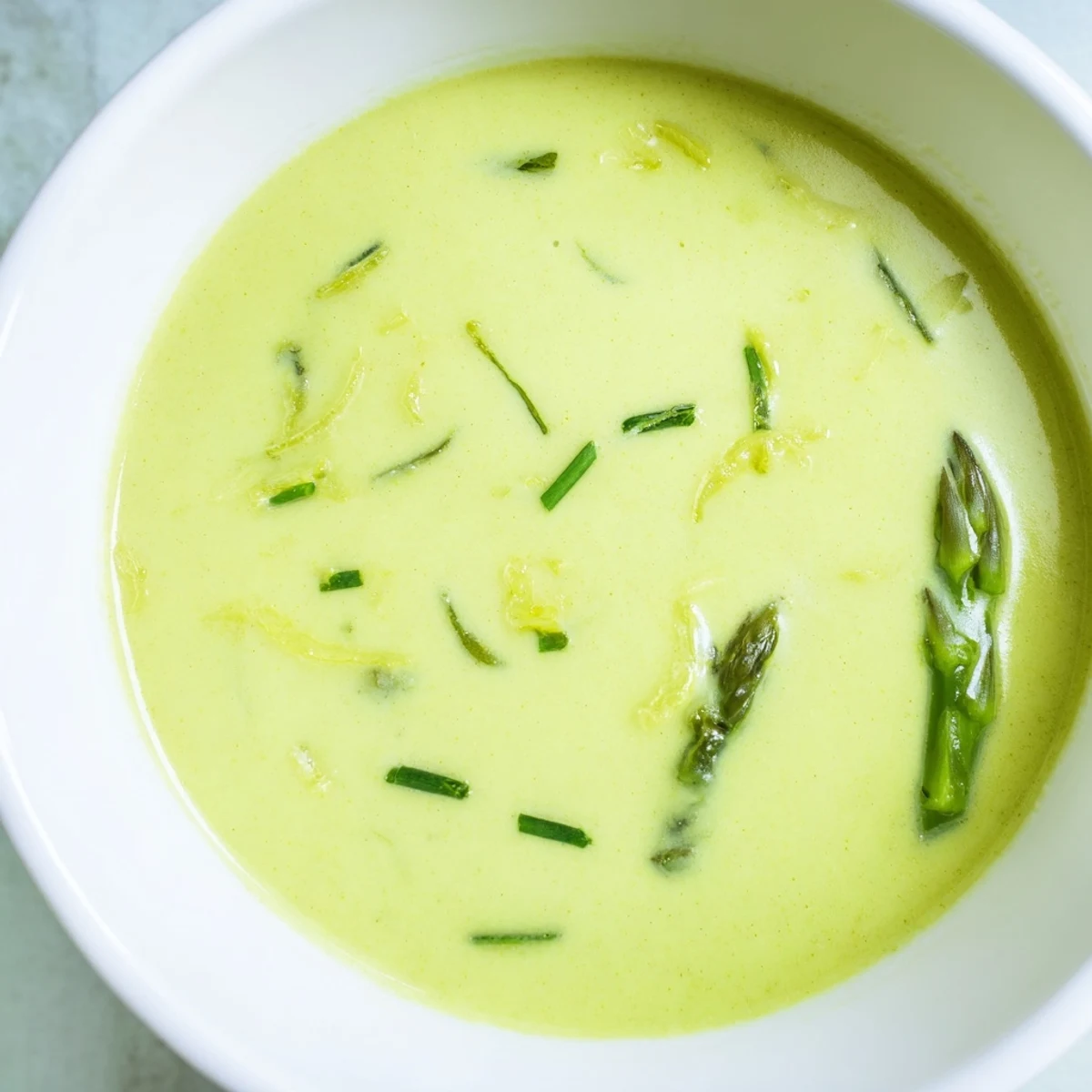 A vibrant green bowl of Creamy Asparagus Soup with Lemon, featuring a swirl of cream and lemon zest.  