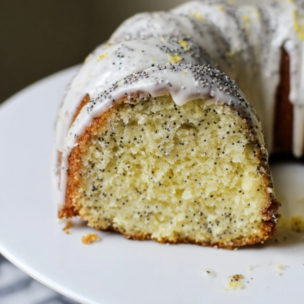A glazed Lemon Poppy Seed Bundt cake, finished with a drizzle and fresh lemon zest, sits ready to serve.