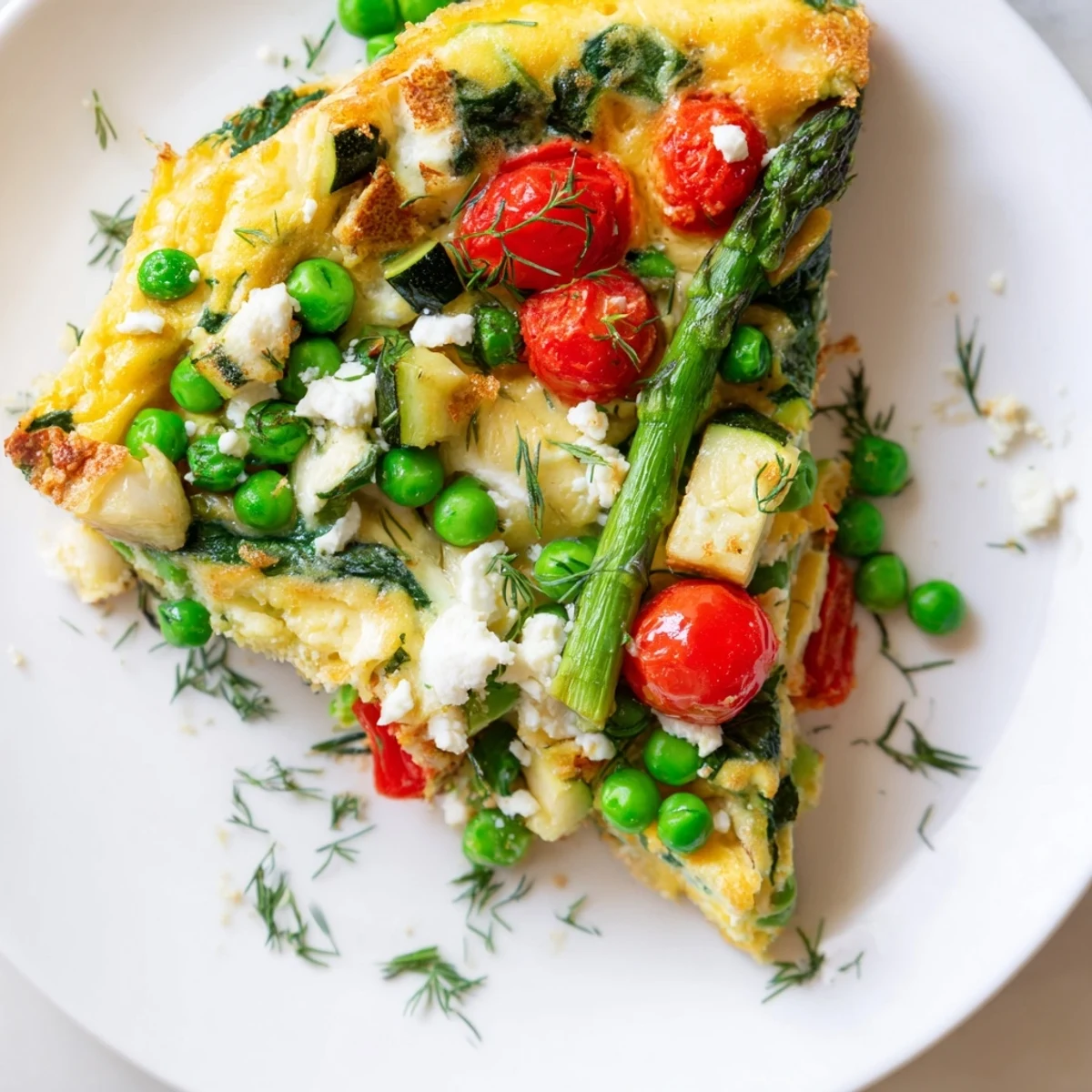 A slice of Spring Vegetable Frittata with Fresh Herbs on a white plate, showcasing vibrant asparagus and peas.