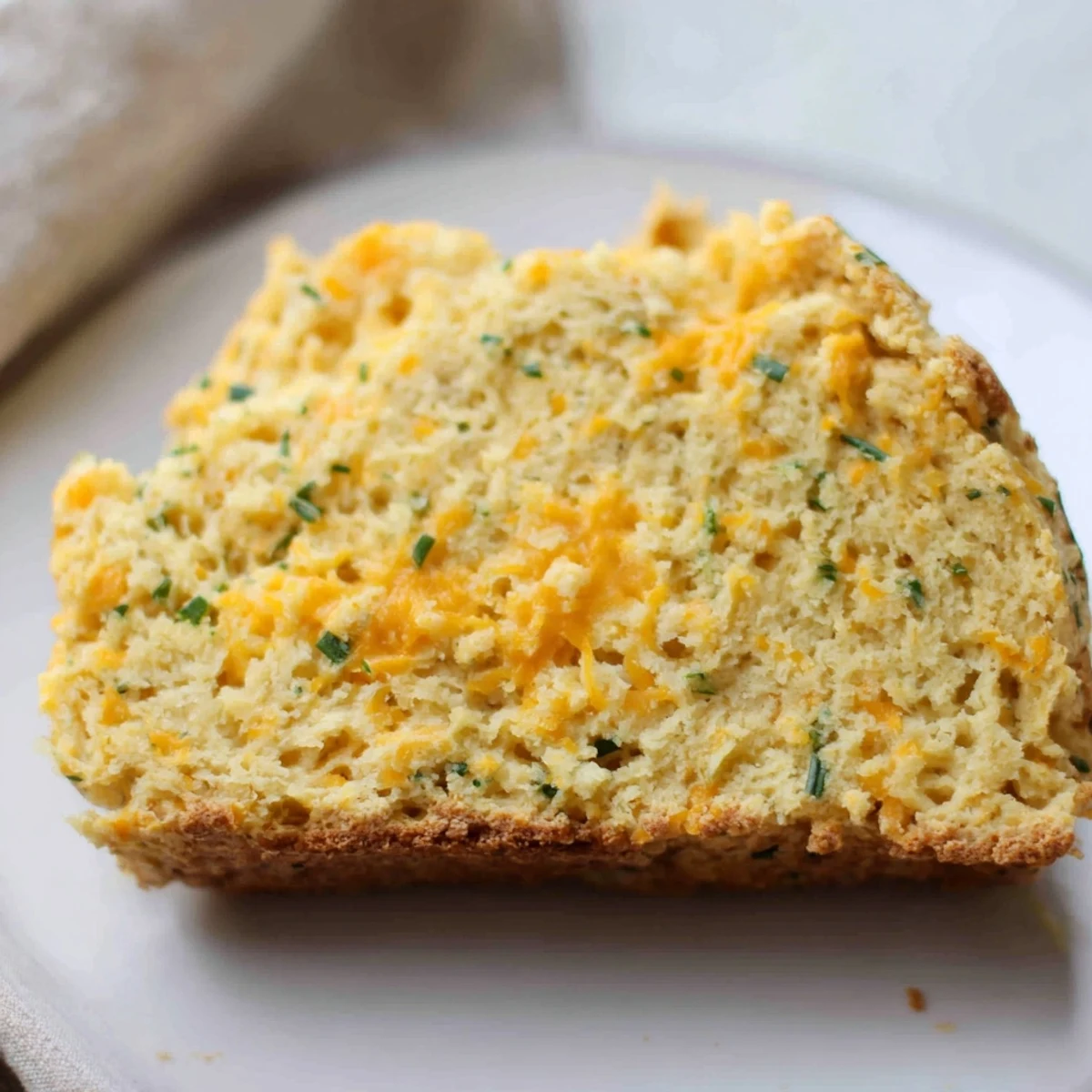Sliced Savory Cheddar & Chive Irish Soda Bread showing a tender, cheesy crumb and herbs.