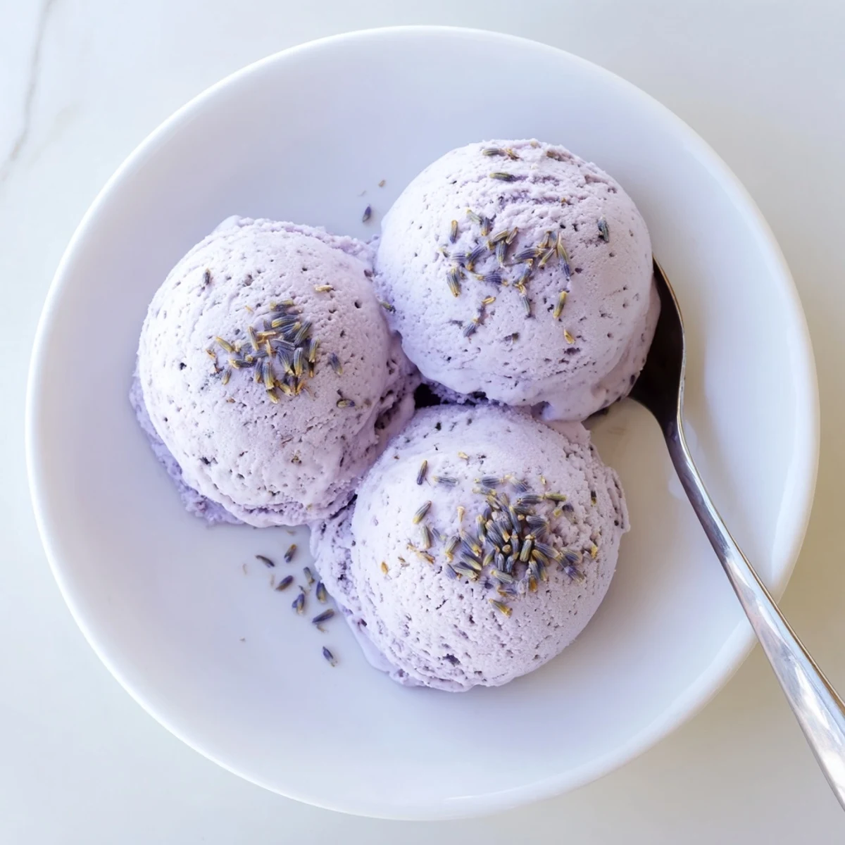 A scoop of Lavender Ice Cream with delicate purple hue sits beside fresh berries and shortbread cookies.