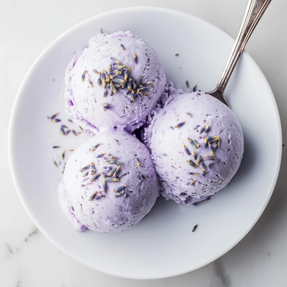 Close-up view of Lavender Ice Cream being scooped from a container, showing creamy texture and floral specks.