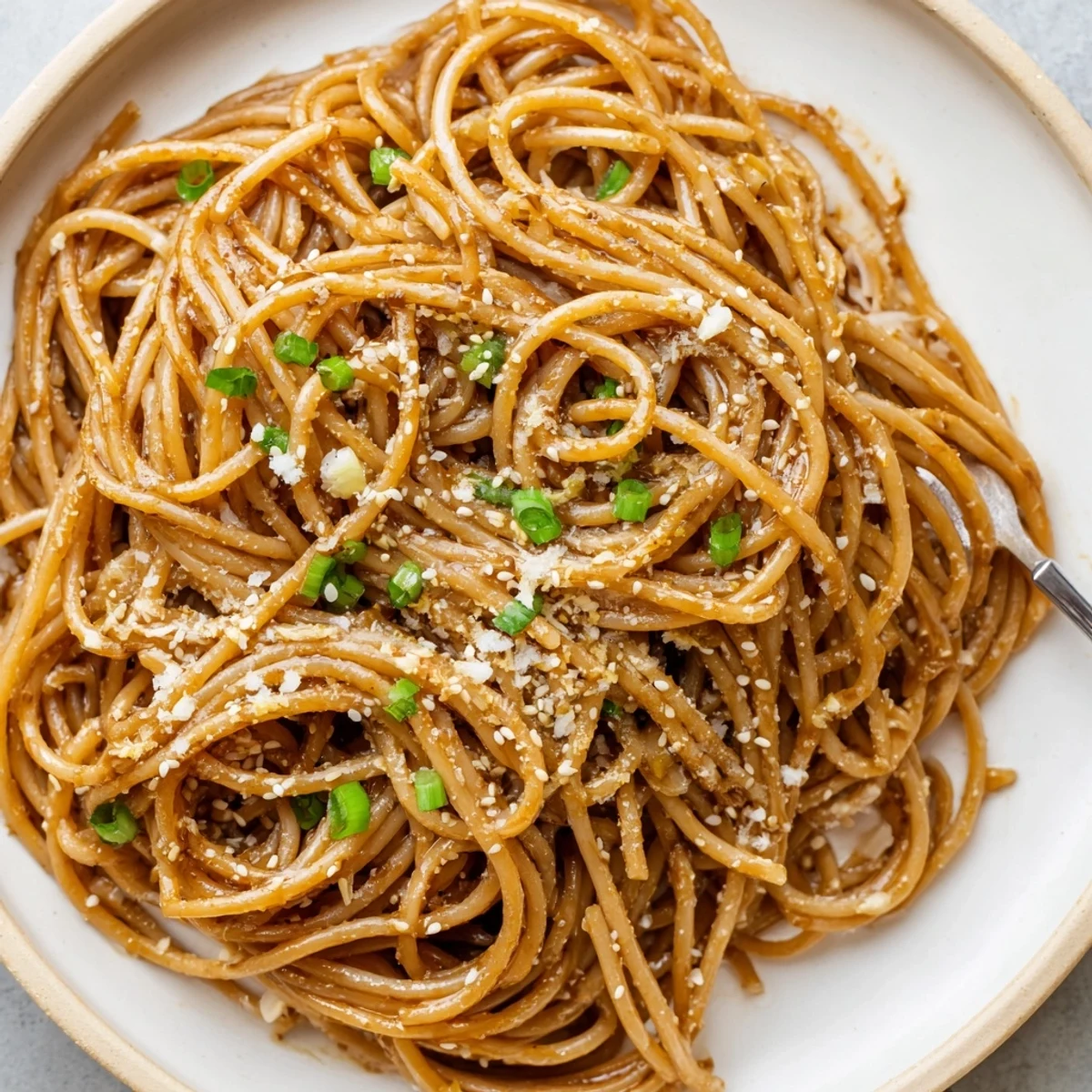 A close-up of Garlic Noodles on a skillet, garnished with scallions and sesame seeds, ready to serve.