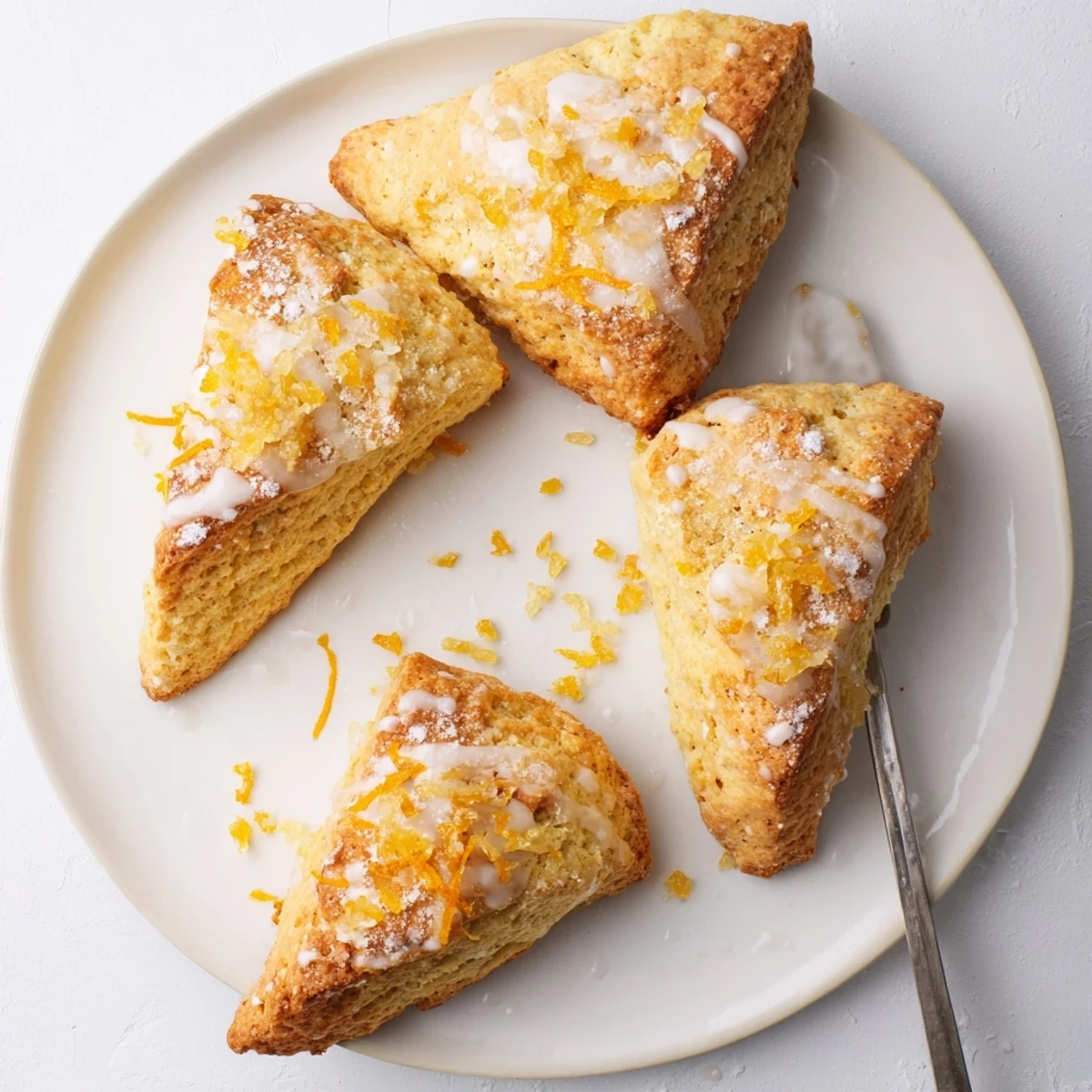 A close-up of Candied Ginger Orange Scones drizzled with glossy orange glaze and paired with steaming tea.
