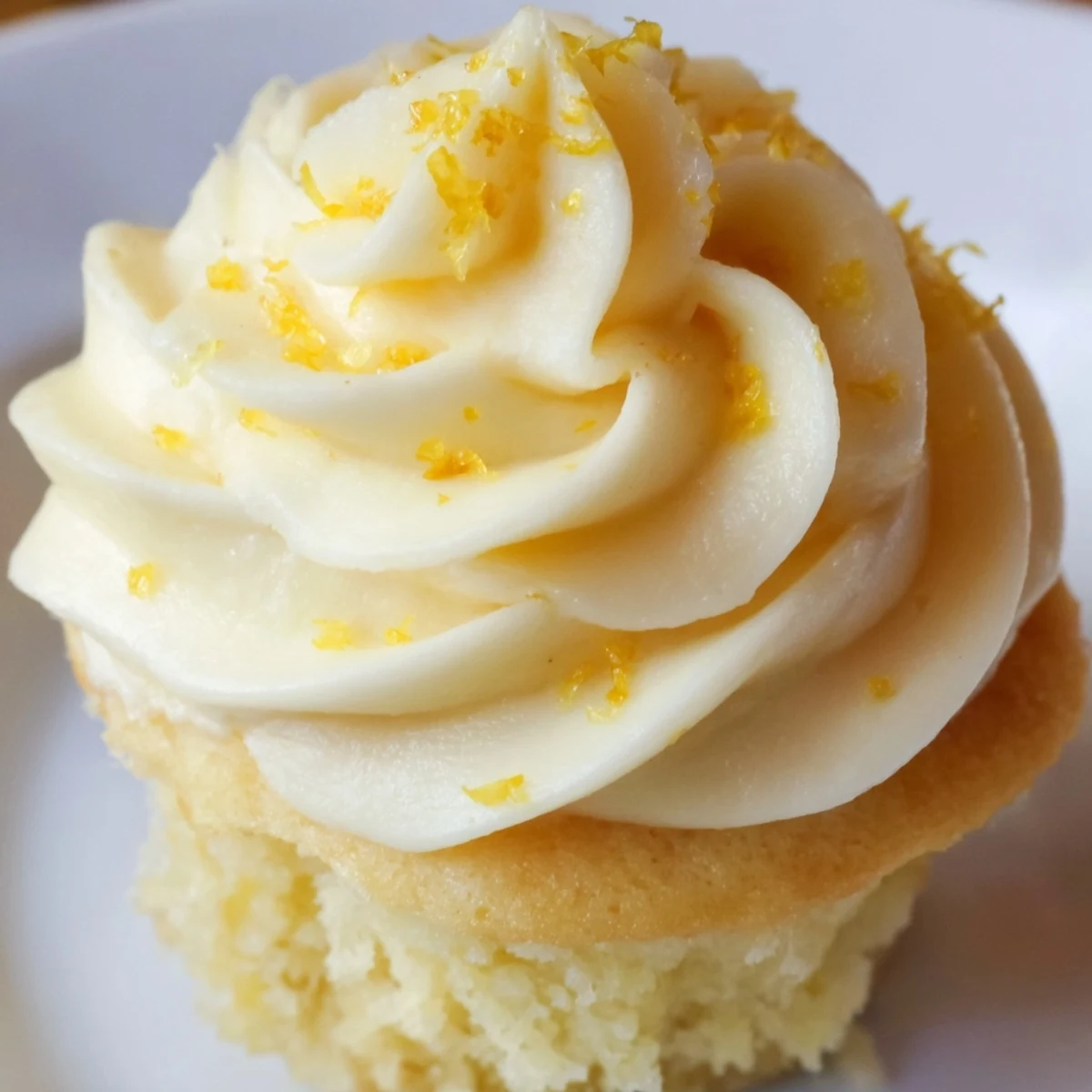 A close-up of homemade Limoncello Cupcakes with fluffy lemon buttercream swirls and zest garnish on a rustic table.