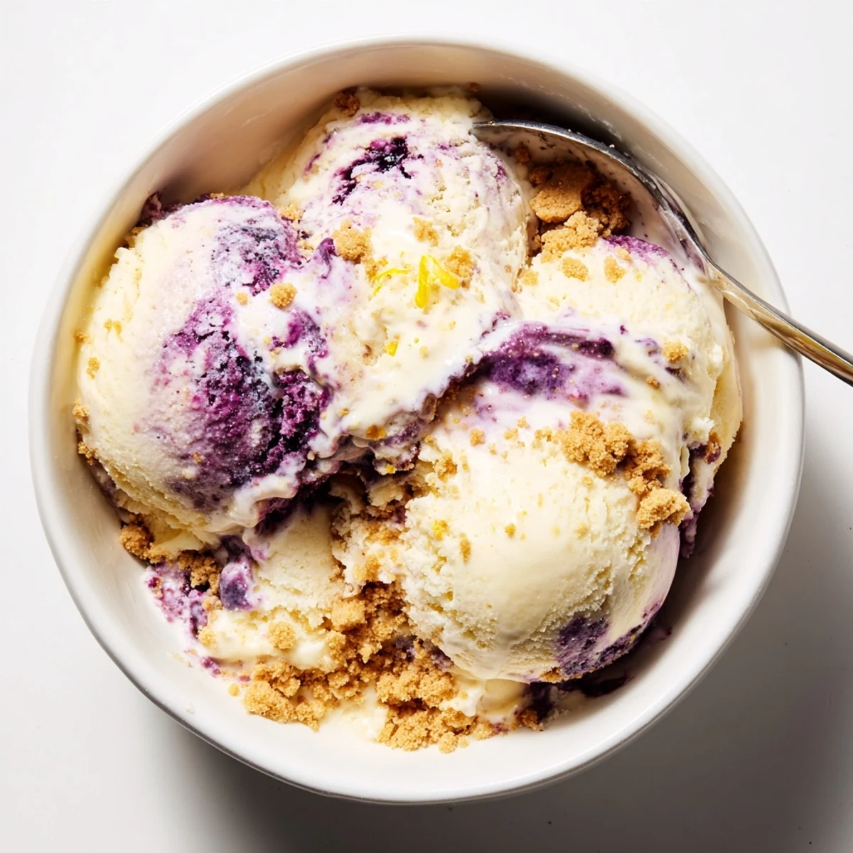 A close-up of Lemon Blueberry Cheesecake Ice Cream swirls with blueberry sauce in a serving dish.