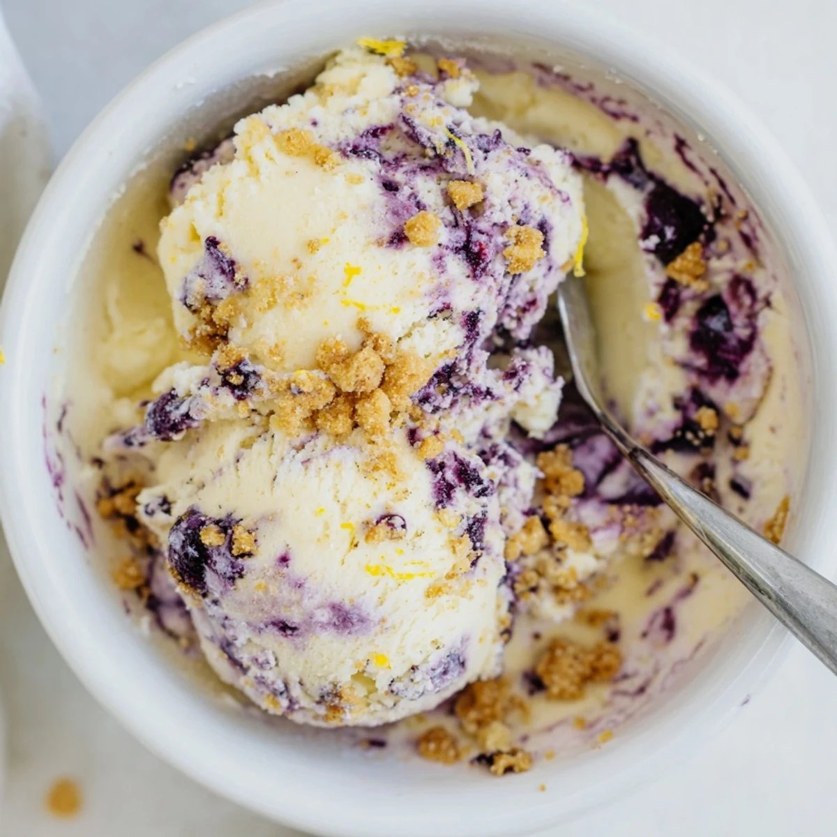 Homemade Lemon Blueberry Cheesecake Ice Cream with lemon zest and blueberry toppings on a summer table.