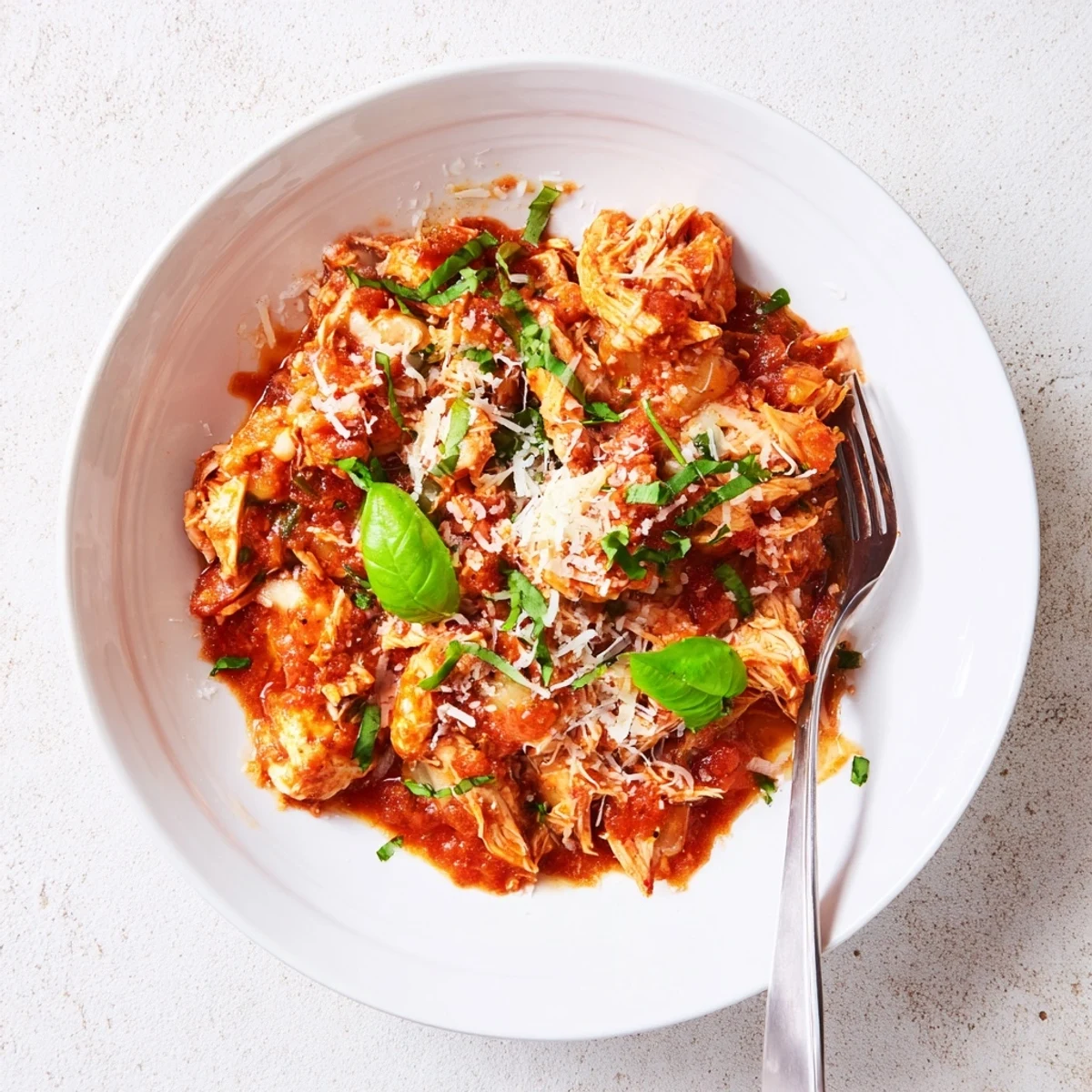 Slow cooker tomato basil chicken steams tenderly in a rich red sauce flecked with fresh green basil leaves.