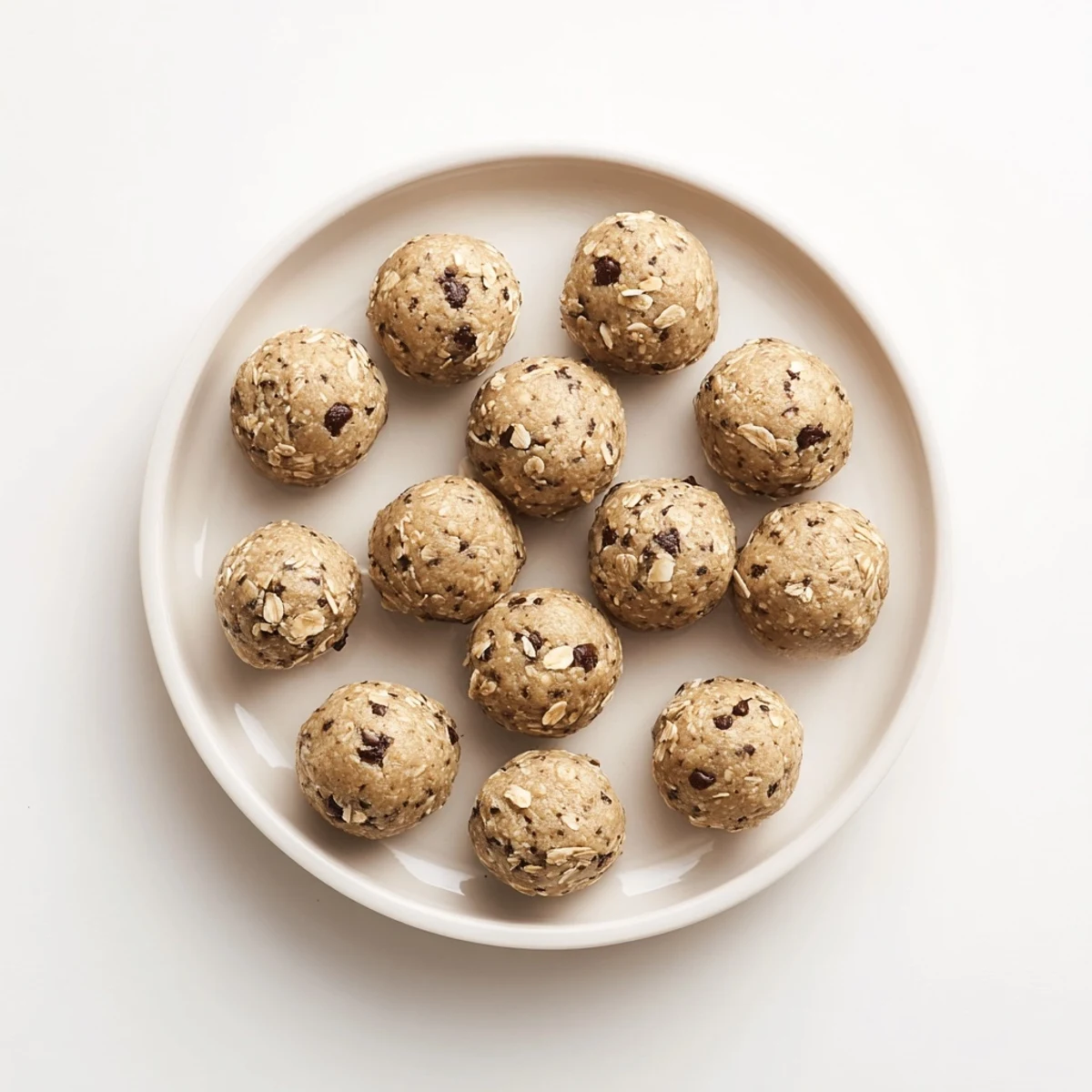 Twelve mint chocolate chip protein balls arranged on a chilled white plate, showing no-bake snack texture.  