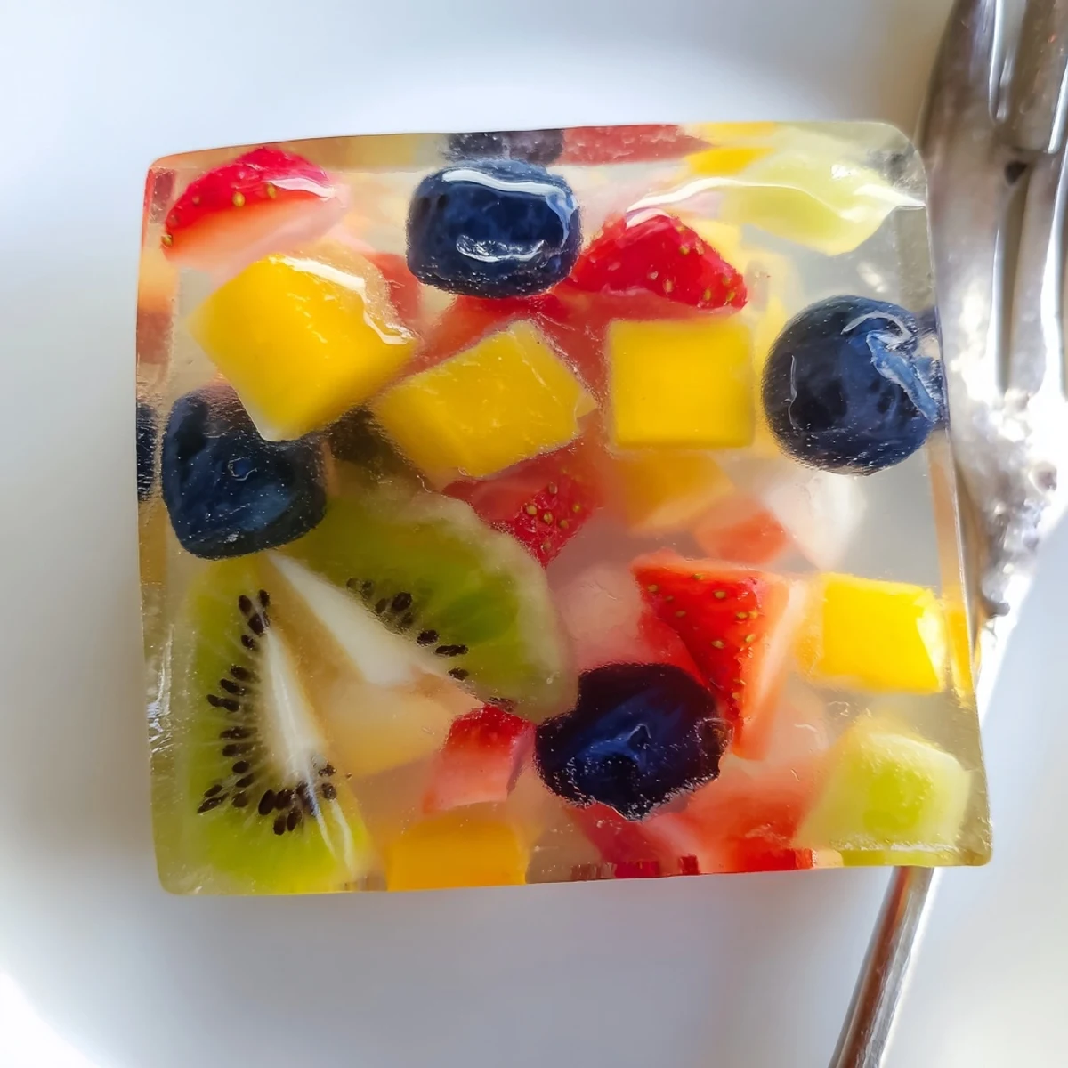 Vegan agar agar fruit jelly cubes arranged on white plate featuring fresh pineapple and blueberries in translucent gelatin