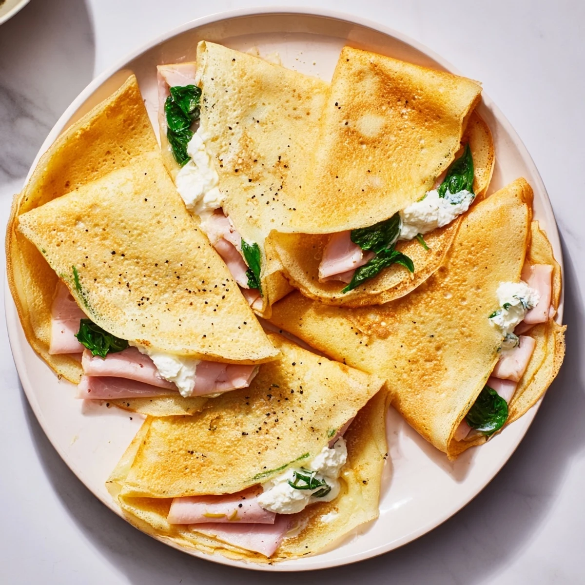 Breakfast savory crepes rolled around ham and fresh spinach, topped with golden melted Swiss cheese