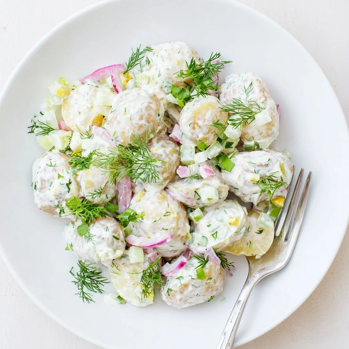 Creamy Greek yogurt potato salad with tender baby potatoes, fresh herbs, and crisp colorful vegetables in a rustic serving bowl.