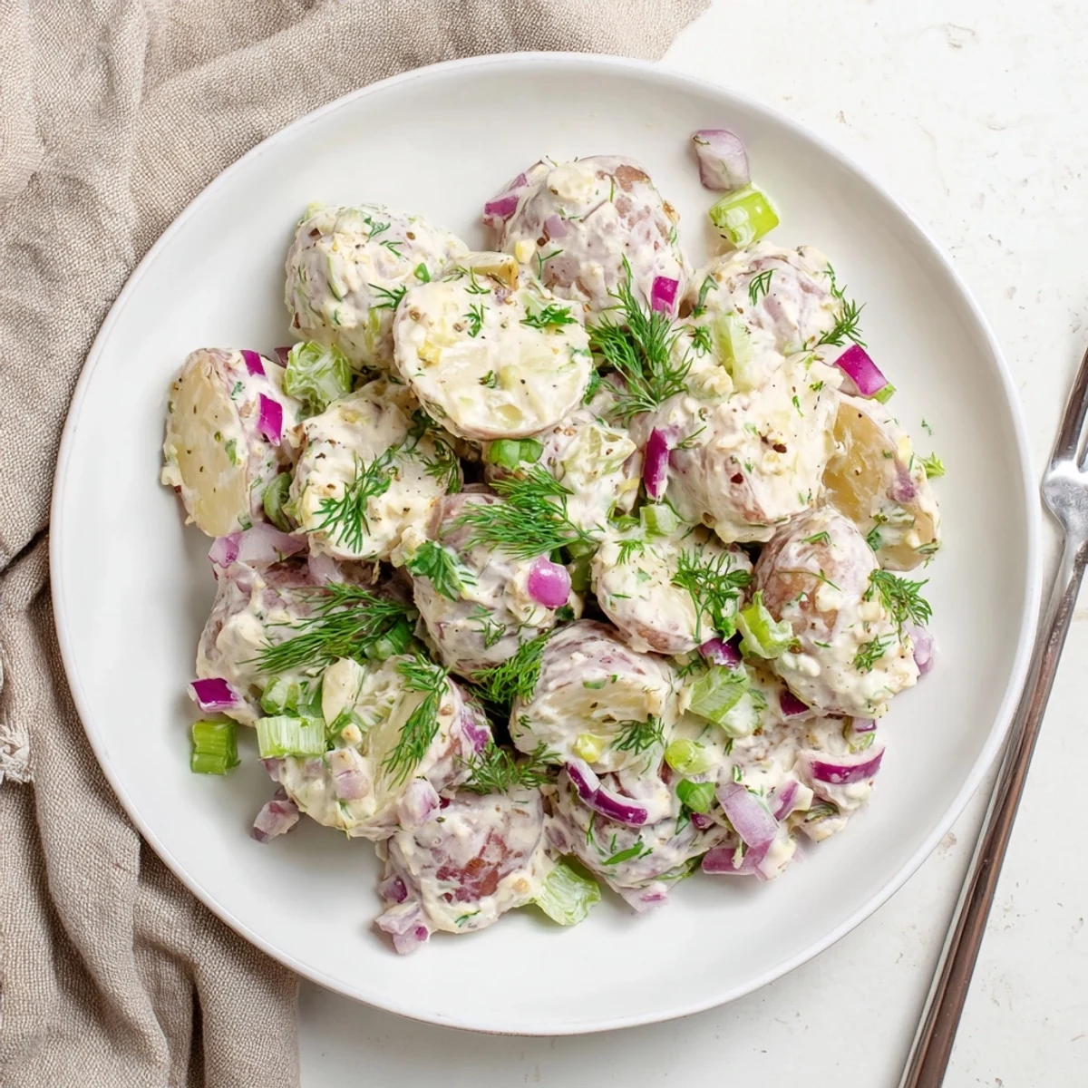 Lightened-up Greek yogurt potato salad featuring red-skinned potatoes tossed in tangy dressing with dill, parsley, and diced crunchy vegetables.