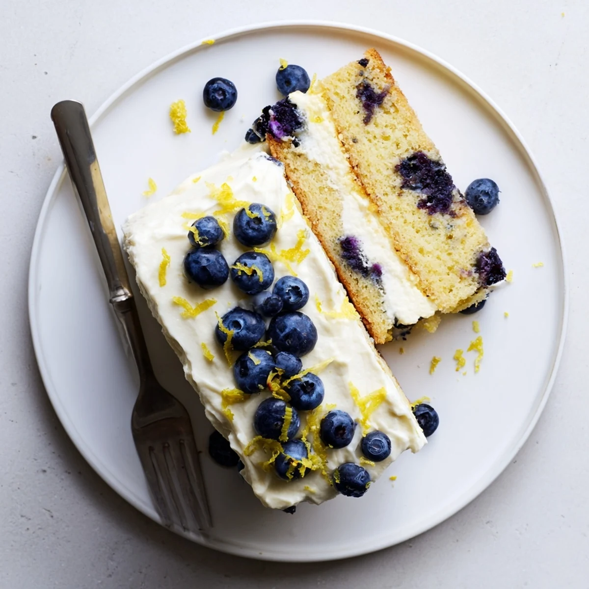 Moist lemon blueberry cake layered with tangy cream cheese frosting topped with scattered blueberries and lemon zest