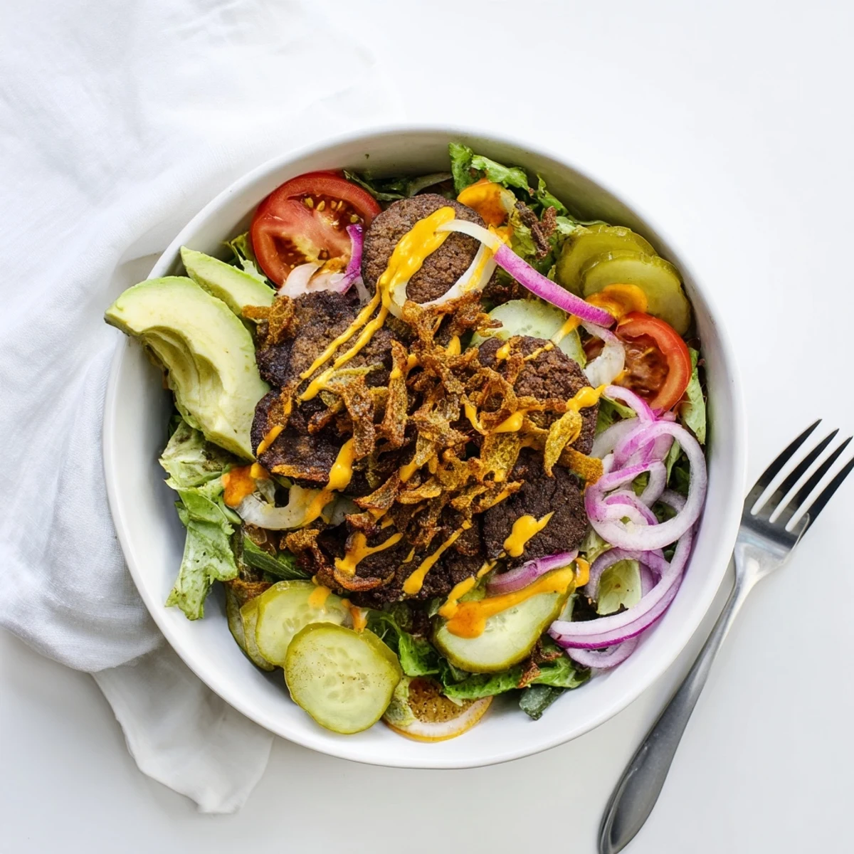 Deconstructed smash burger bowl featuring juicy beef crumbles, ripe avocado slices, tangy pickles, and drizzled creamy sauce