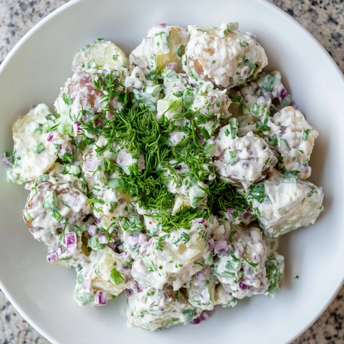 Creamy Greek yogurt potato salad with tender red potatoes, crunchy celery, and fresh green herbs in a white serving bowl