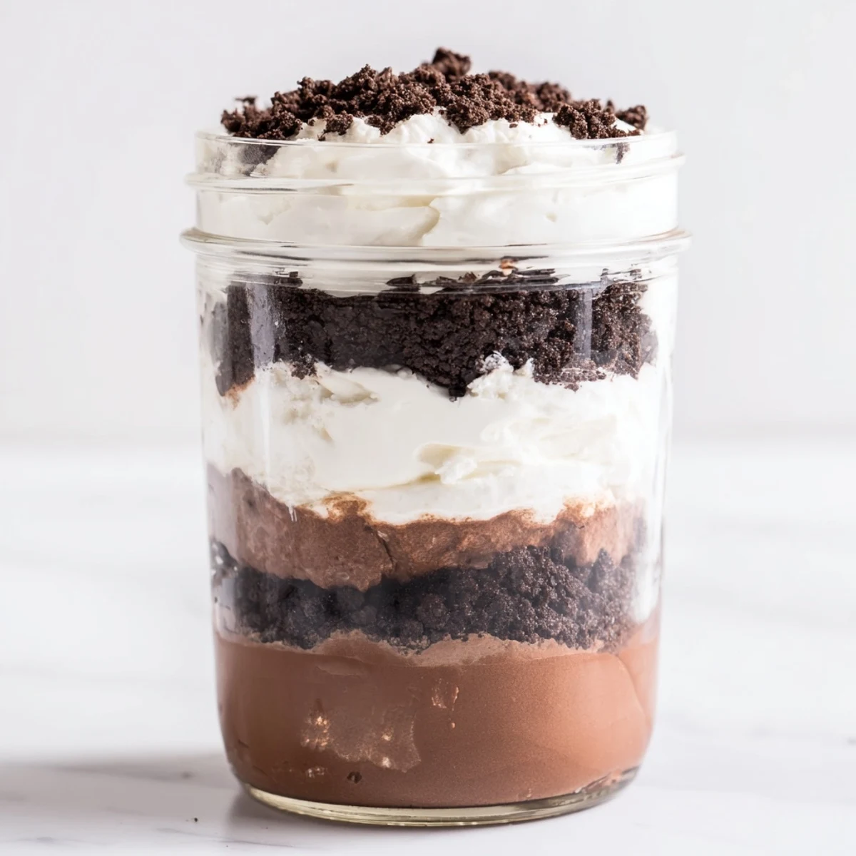 Glass bowl layered with creamy keto dirt cake showing chocolate pudding and whipped cream beneath dark chocolate almond crumble topping