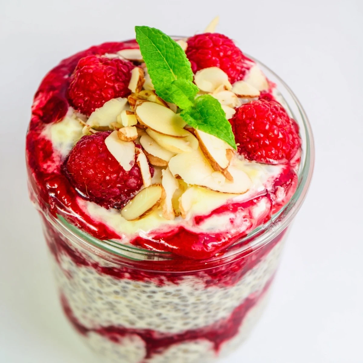Glass jar showing layered raspberry chia pudding sweetened naturally with maple syrup and almond milk