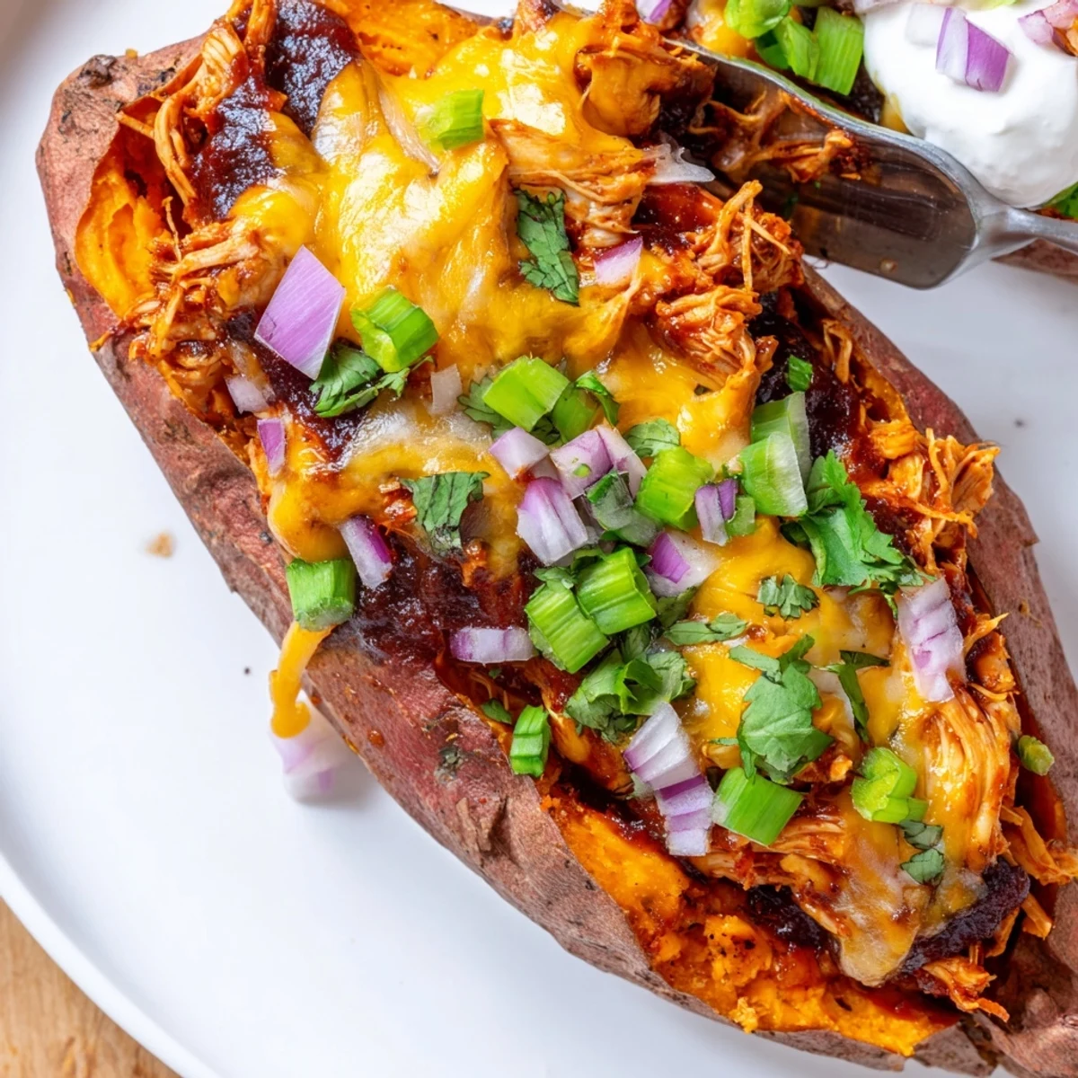 BBQ chicken stuffed sweet potatoes topped with green onions and a creamy sour cream dollop