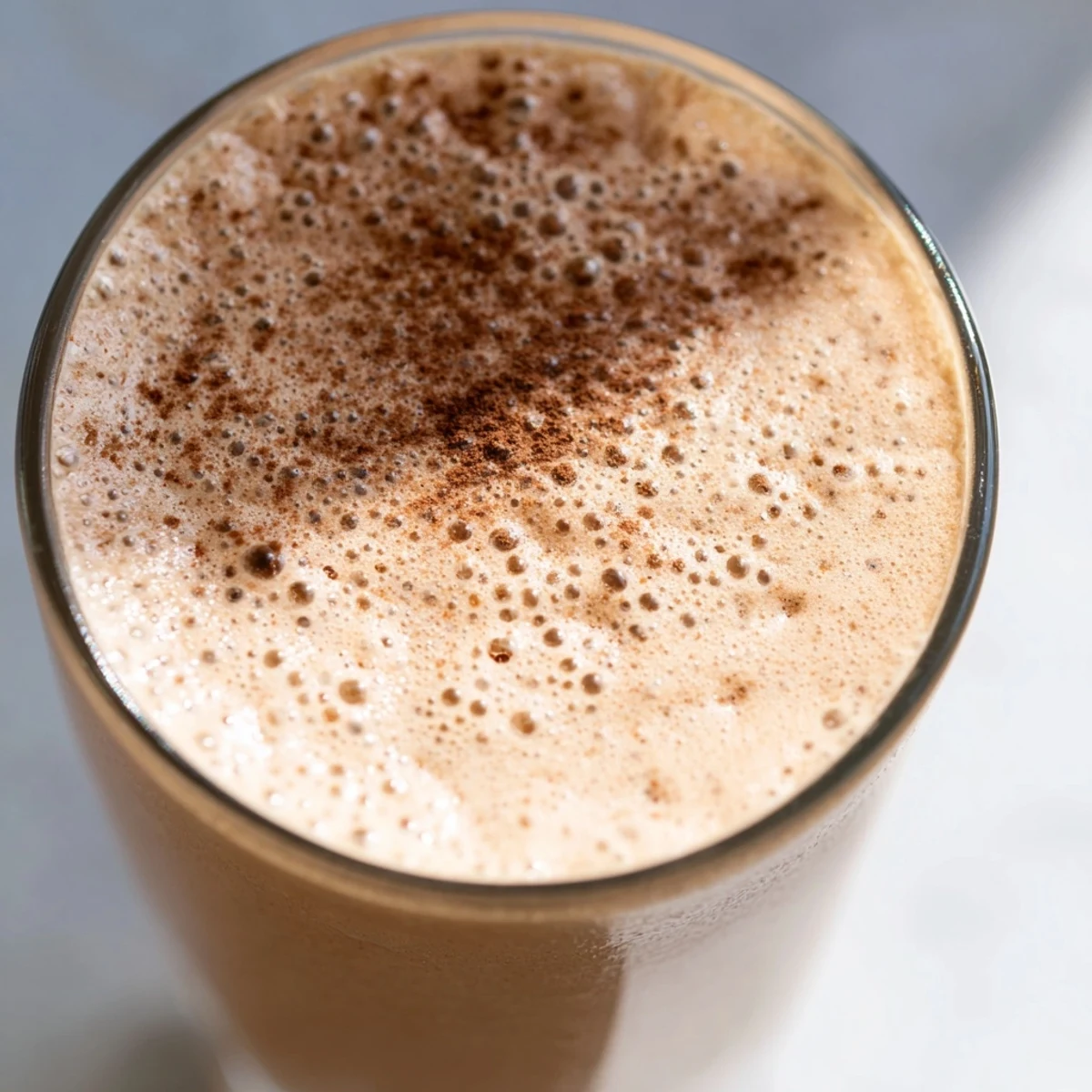 Creamy coffee smoothie in a glass topped with a sprinkle of cinnamon