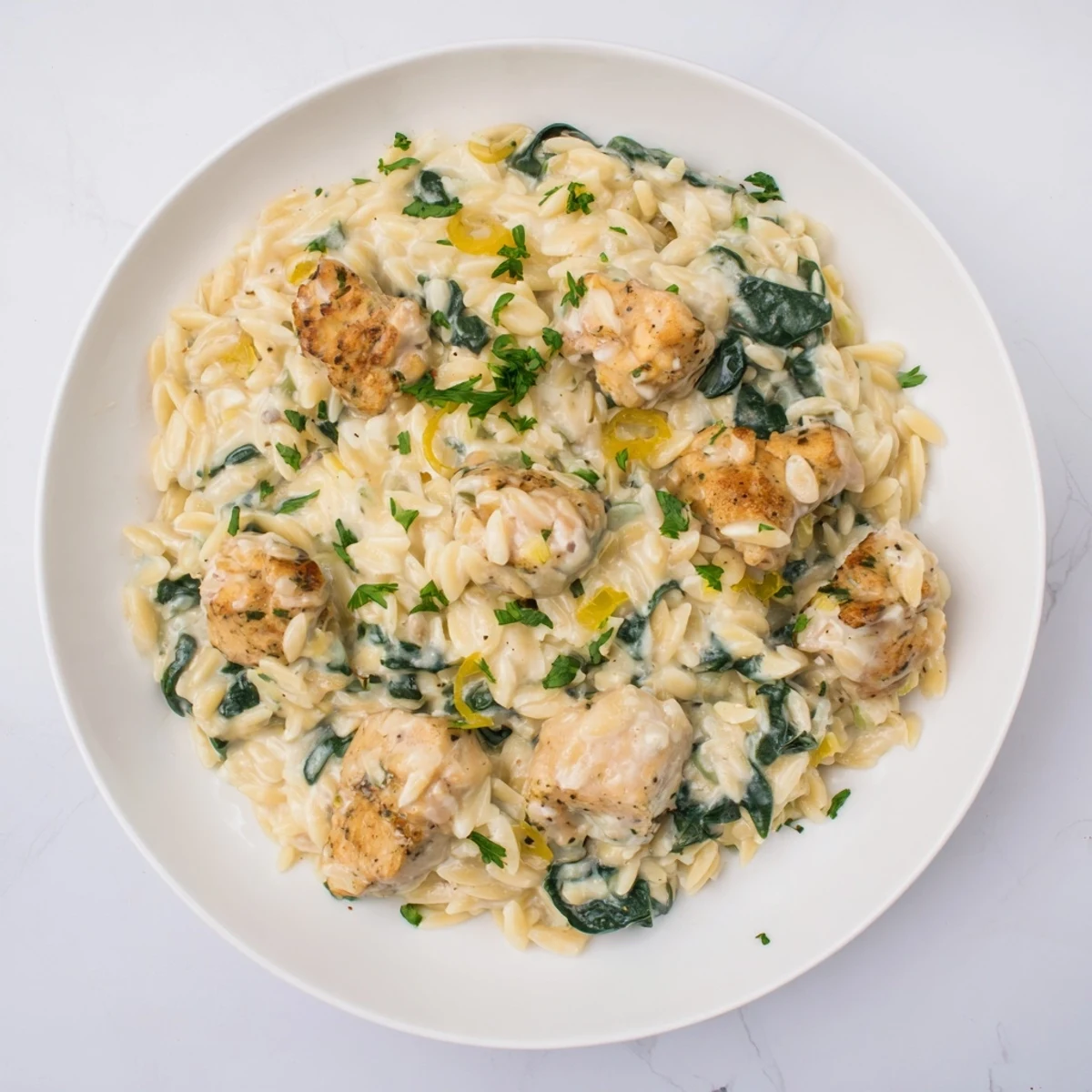 Golden chicken pieces nestled in creamy Boursin orzo with fresh wilted spinach in a skillet.