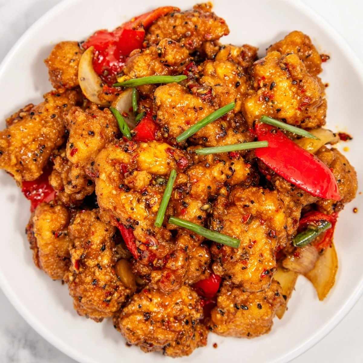 Asian-inspired crispy pepper chicken dish featuring tender fried bites with red peppers and green onions