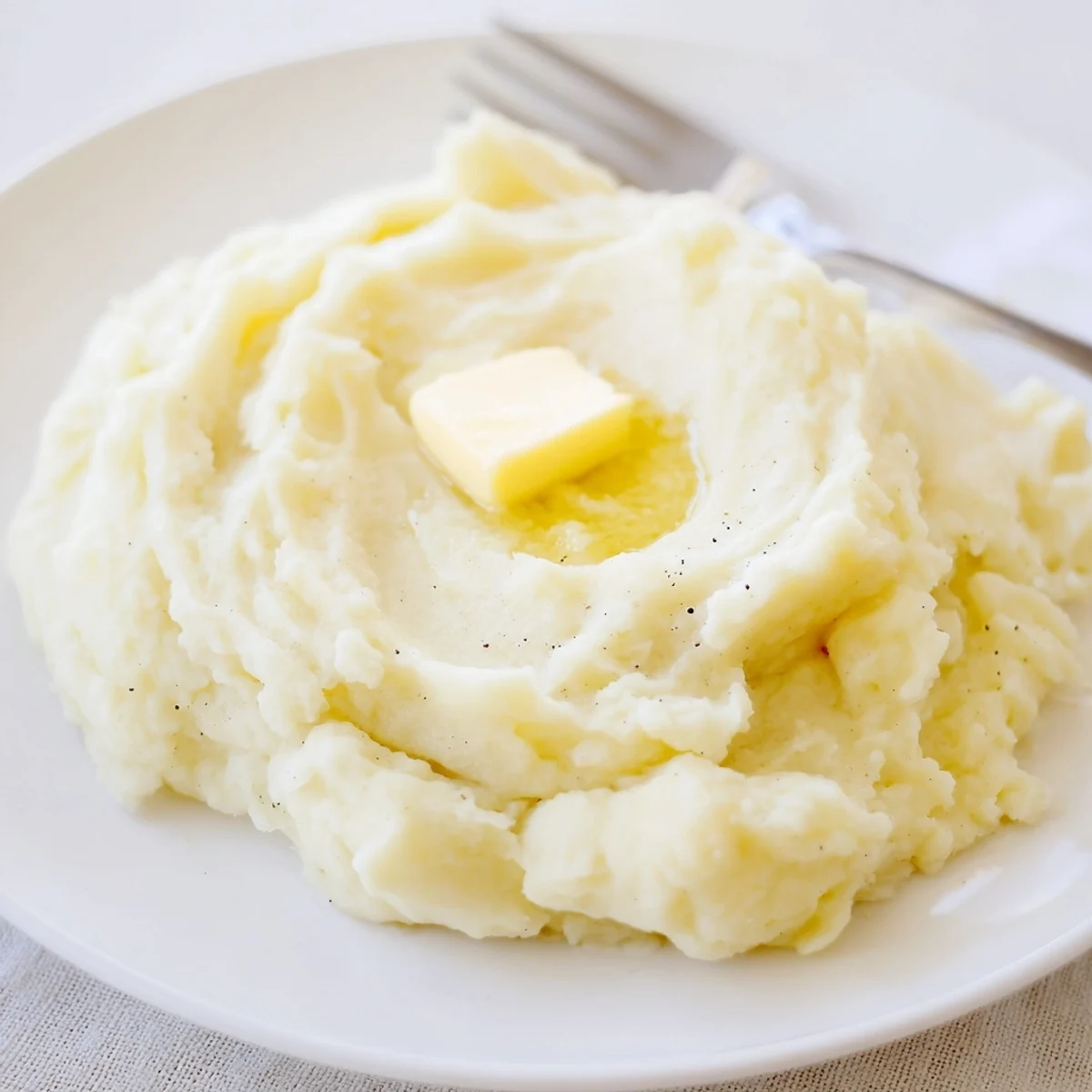 Steaming bowl of Velvety Mashed Potatoes garnished with cracked pepper and fresh chives