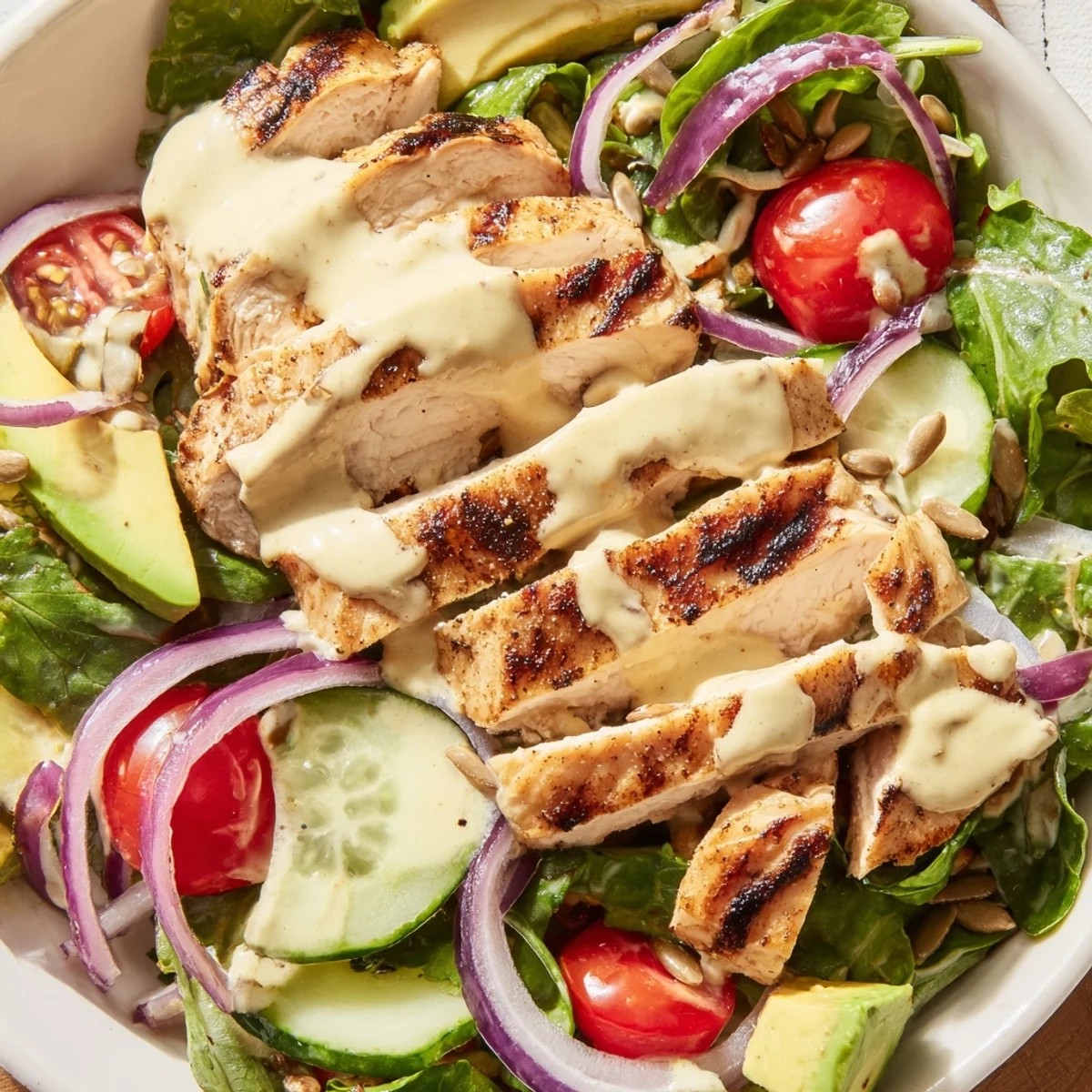 Sliced chicken breast nestled atop fresh greens with creamy honey mustard dressing cascading over ripe avocado