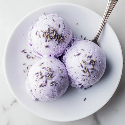 Close-up view of Lavender Ice Cream being scooped from a container, showing creamy texture and floral specks.