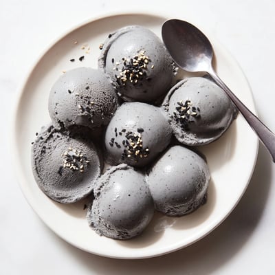 The smooth texture of Toasted Black Sesame Ice Cream is visible on a chilled ceramic plate, garnished with extra toasted seeds for a nutty crunch.