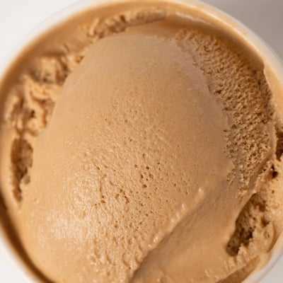 A close-up of homemade Hojicha Ice Cream in a waffle cone, showing its smooth texture and roasted green tea flavor in warm lighting.