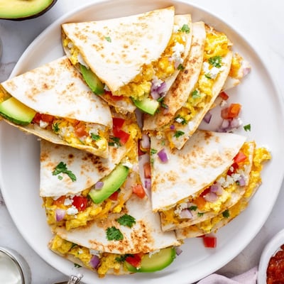 Spicy Avocado Egg and Three Cheese Quesadillas are folded and served warm on a rustic wooden board with fresh cilantro garnish.